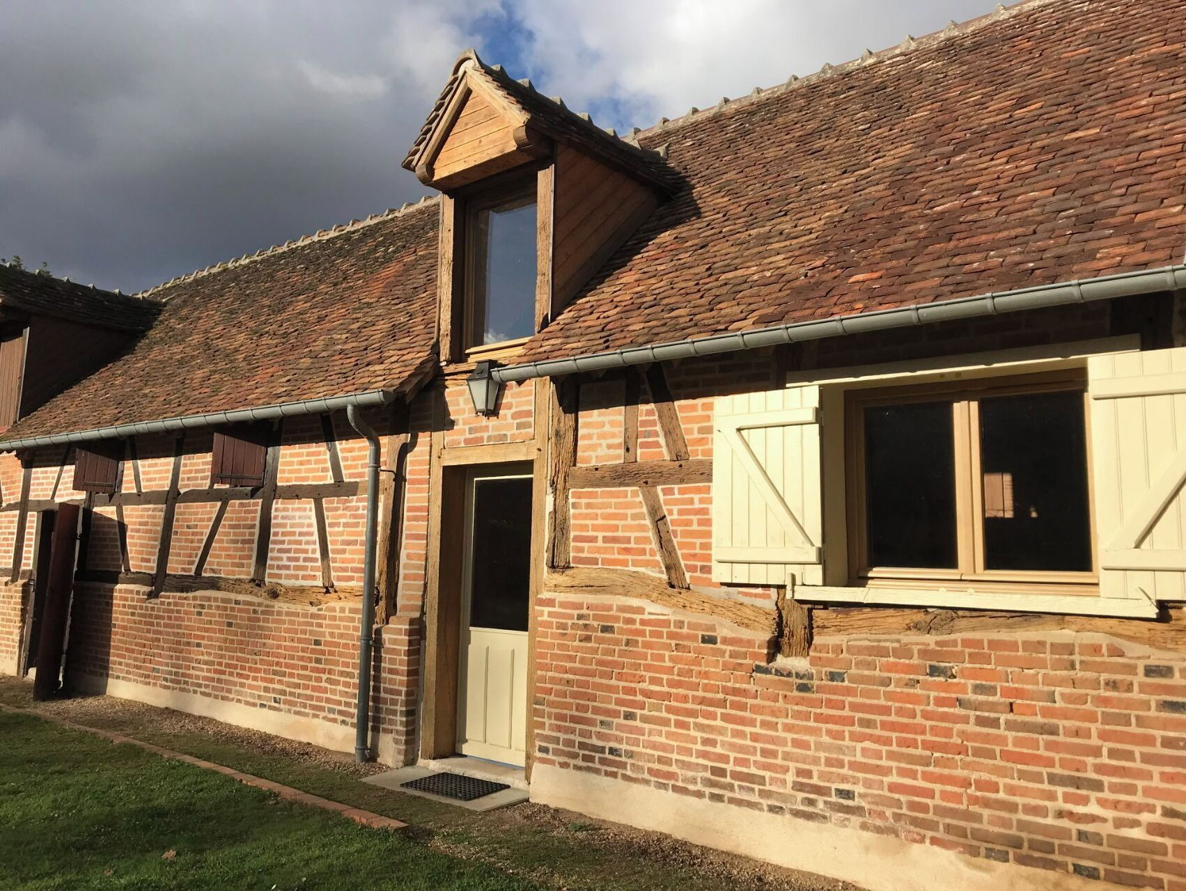 A traditional brick building with a sloped roof, wooden shutters, and a small window.