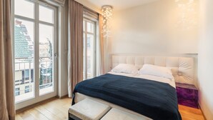 A bedroom with a large window, a bed with a dark bedspread, a headboard, and a bedside table. - Grand Apartments - Willa Morska (Sopot)