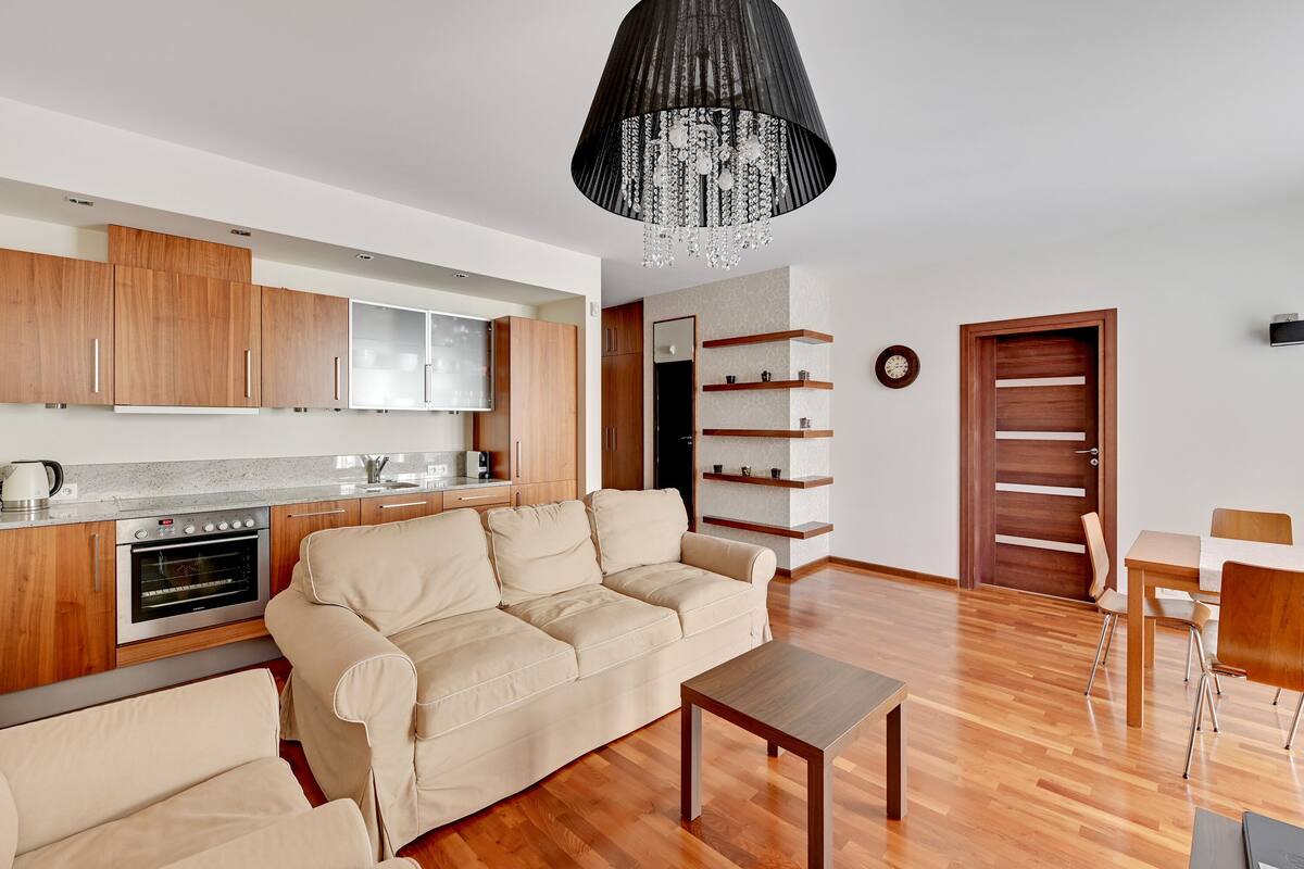 A modern kitchen with wooden cabinets, a beige sofa, and a dining area with a table and chairs.