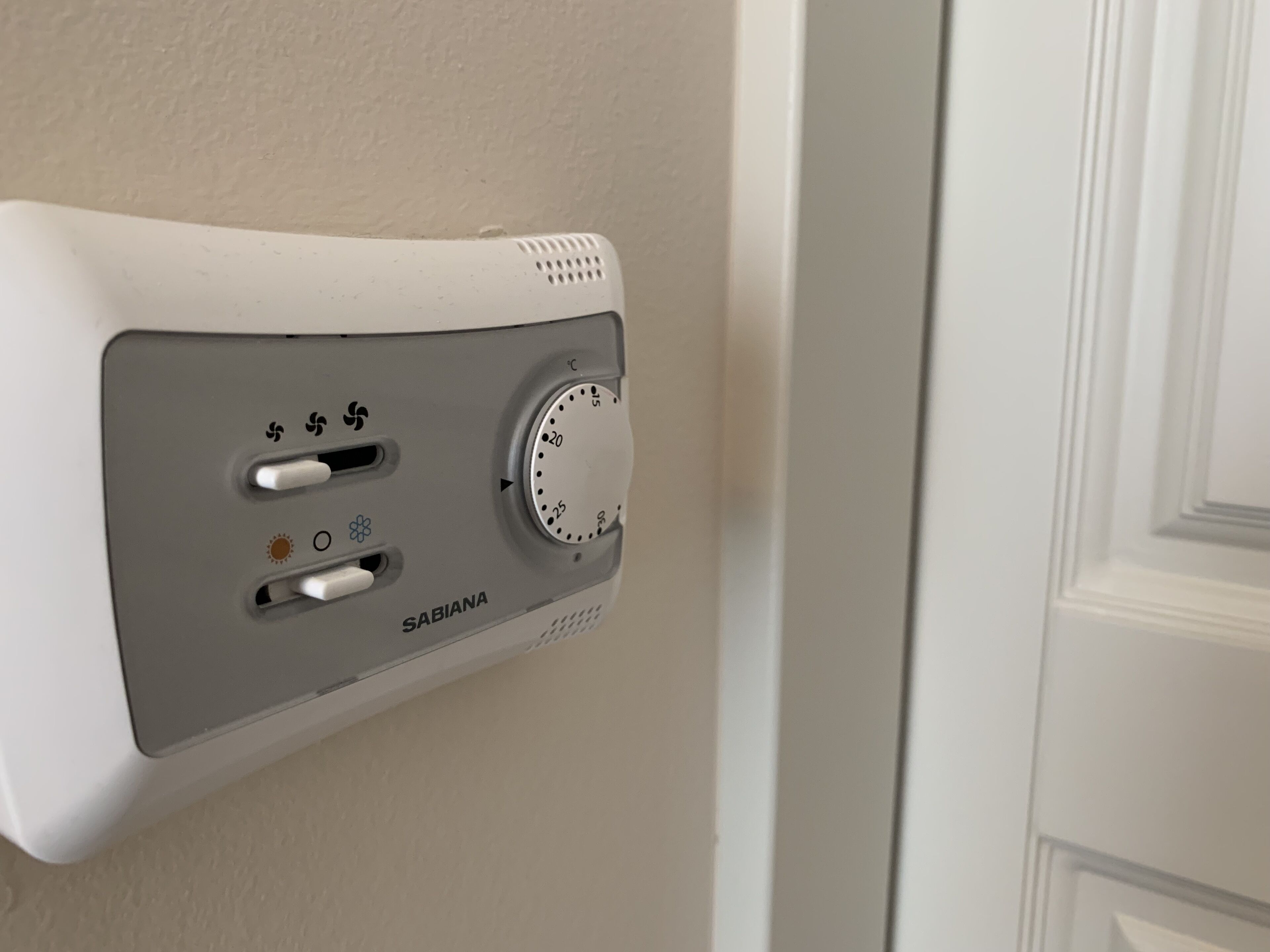 A wall-mounted thermostat with a temperature control dial and two switches, labeled "SABIANA."