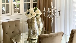 A dining area with a glass table, cushioned chairs, a decorative candelabra, and a geometric chandelier. - Lakeside condo with beach access (Csopak)