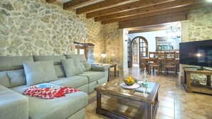 A living room with a stone wall, a sofa, a coffee table with a fruit bowl, and a television on a wooden stand. - VILLA PLOMER - 2 MIN WALK TO THE OLD TOWN (Pollensa)