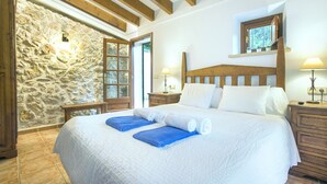 A bedroom with a stone wall, wooden beams, a large bed with white linens, two nightstands, and a window with a view. - VILLA PLOMER - 2 MIN WALK TO THE OLD TOWN (Pollensa)
