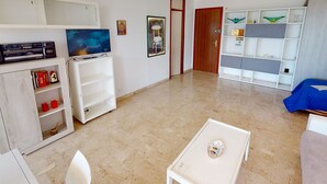 A modern living room with a flat-screen TV, a bookshelf, a small table, and a door leading to another room. - Spacious studio in Menton with large terrace and garage (Menton)