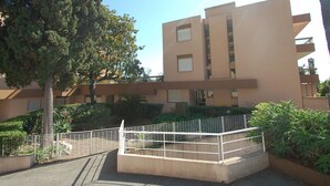 A multi-story building with a flat roof, surrounded by greenery and a metal fence. - Spacious studio in Menton with large terrace and garage (Menton)