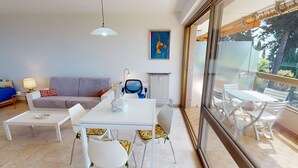 A modern living room with a dining area, a sofa, a table, and chairs. There is a radiator, a lamp, and a painting on the wall. - Spacious studio in Menton with large terrace and garage (Menton)