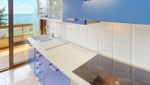 A modern kitchen with a large window, white countertops, blue cabinets, and a view of the sea. - Spacious studio in Menton with large terrace and garage (Menton)