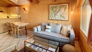 Un intérieur chaleureux en bois, avec un coin repas, un canapé et une table basse sur laquelle sont posés des livres.