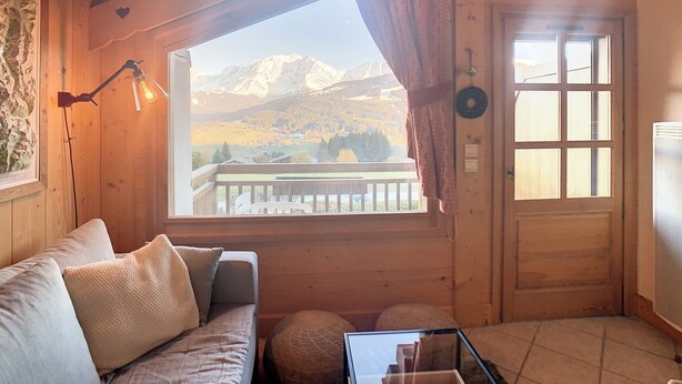 L’intérieur d’un chalet en bois, avec un canapé, une table, une fenêtre donnant sur les montagnes et une porte.
