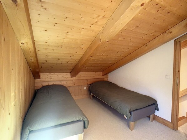 A small attic bedroom with two single beds, wooden beams, and a sloped ceiling. - 4-room duplex with parking and wifi at the foot of the slopes (Combloux)