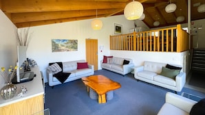 Ein geräumiger Wohnbereich mit zwei Sofas, einem Holztisch und einer Treppe, die zu einer oberen Ebene führt.