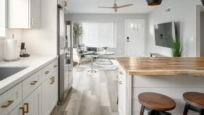 Eine moderne Küche mit weißen Schränken, einer Holz Arbeitsplatte und einem eingebauten Herd. Es gibt einen Essbereich mit Tisch und Stühlen, und einen Deckenventilator darüber.