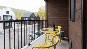 Un balcon avec des chaises jaunes et une table, une bouteille de vin, et une vue sur des immeubles et un parking.