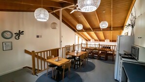 Ein Restaurant mit Holztischen und -stühlen, hängenden Leuchten und einer Wanduhr.
