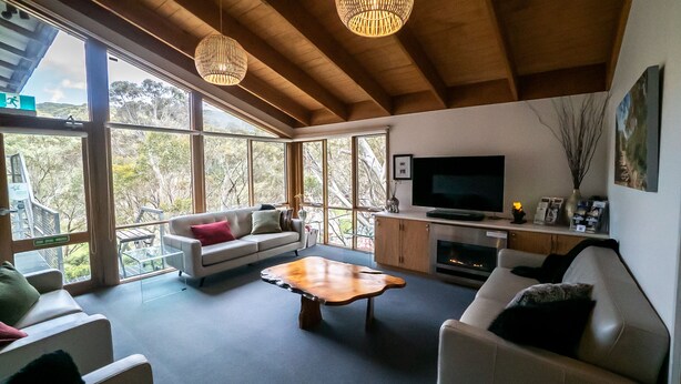 Ein großzügiges Wohnzimmer mit großem Fernseher, bequemen Sitzgelegenheiten, einem Kamin und großen Fenstern mit Blick ins Freie.