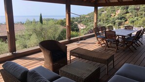 A covered outdoor seating area with wicker furniture and a table, overlooking a scenic landscape with hills and a body of water. - Magnificent sea view villa 500m from the beach and 10min from Porto-Vecchio (Porto-Vecchio)