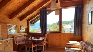 Un chalet confortable aux murs en bois, avec un coin repas comprenant une banquette, un canapé et une grande fenêtre donnant sur les montagnes.