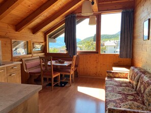 A cozy cabin with wooden walls, a dining area with a bench, a sofa, and a large window offering a mountain view.
