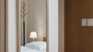Une chambre à coucher avec un lit, une lampe de chevet, un porte-manteau et un miroir qui reflète la pièce.