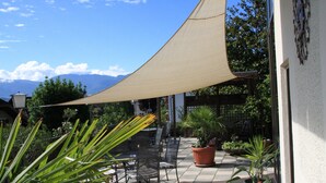 Une terrasse extérieure dotée d’une grande voile d’ombrage, de mobilier d’extérieur, de plantes en pot et offrant une vue sur les montagnes.