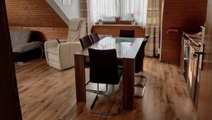 Una habitación acogedora con suelo de madera, una mesa de comedor con sillas, un sofá y una ventana con cortinas.