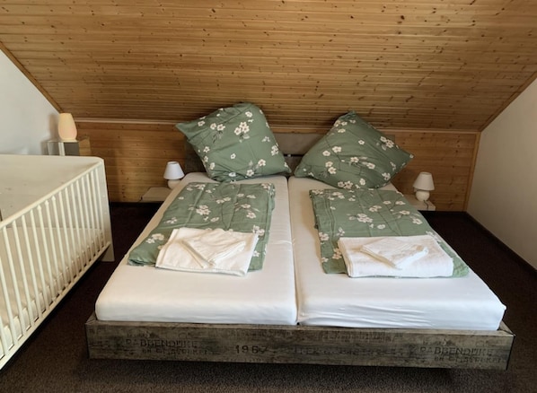 A double bed with floral bedding, two bedside tables with lamps, and a crib.