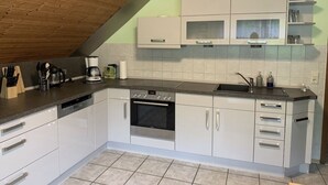 Una cocina moderna con armarios blancos, horno empotrado y encimera con diversos electrodomésticos.