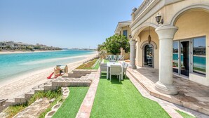 A beachfront property with a patio area featuring outdoor furniture, a children's play area, and a view of the ocean. - Maison Privee - Frond Villa K (Dubai)