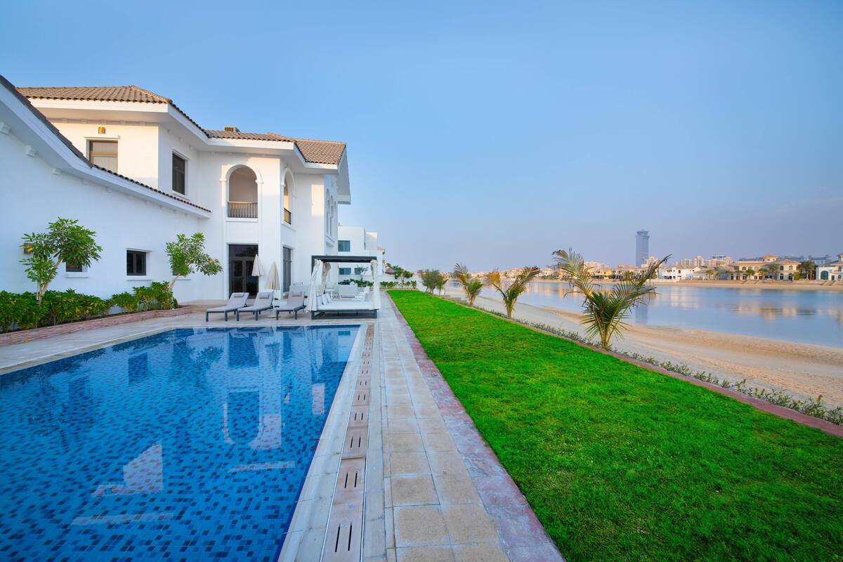 A modern house with a swimming pool, a well-maintained lawn, and a view of a body of water.