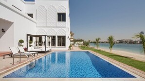 A modern white building with a swimming pool, lounge chairs, and a view of the sea. - Maison Privee - Frond Villa K (Dubai)