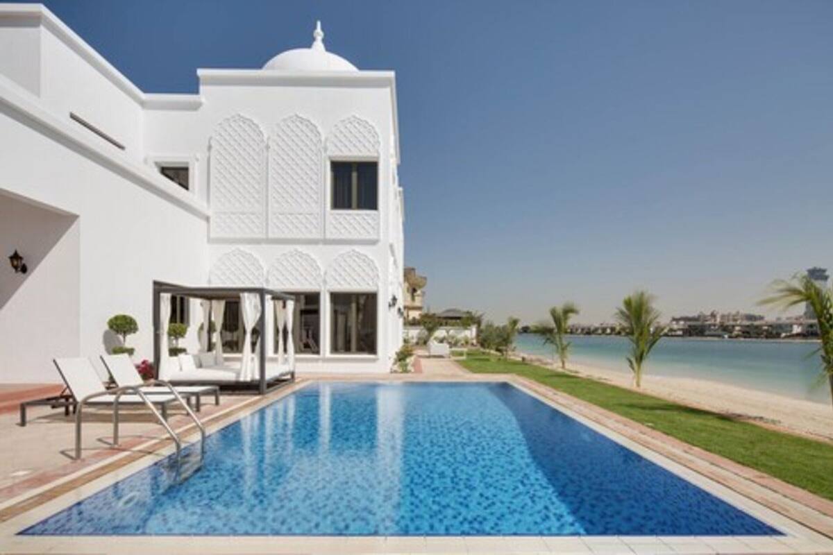 A modern white building with a swimming pool, lounge chairs, and a view of the sea.