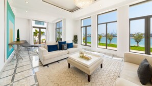 A spacious living room with a large window, a chandelier, and a view of the city. - Maison Privee - Frond Villa K (Dubai)