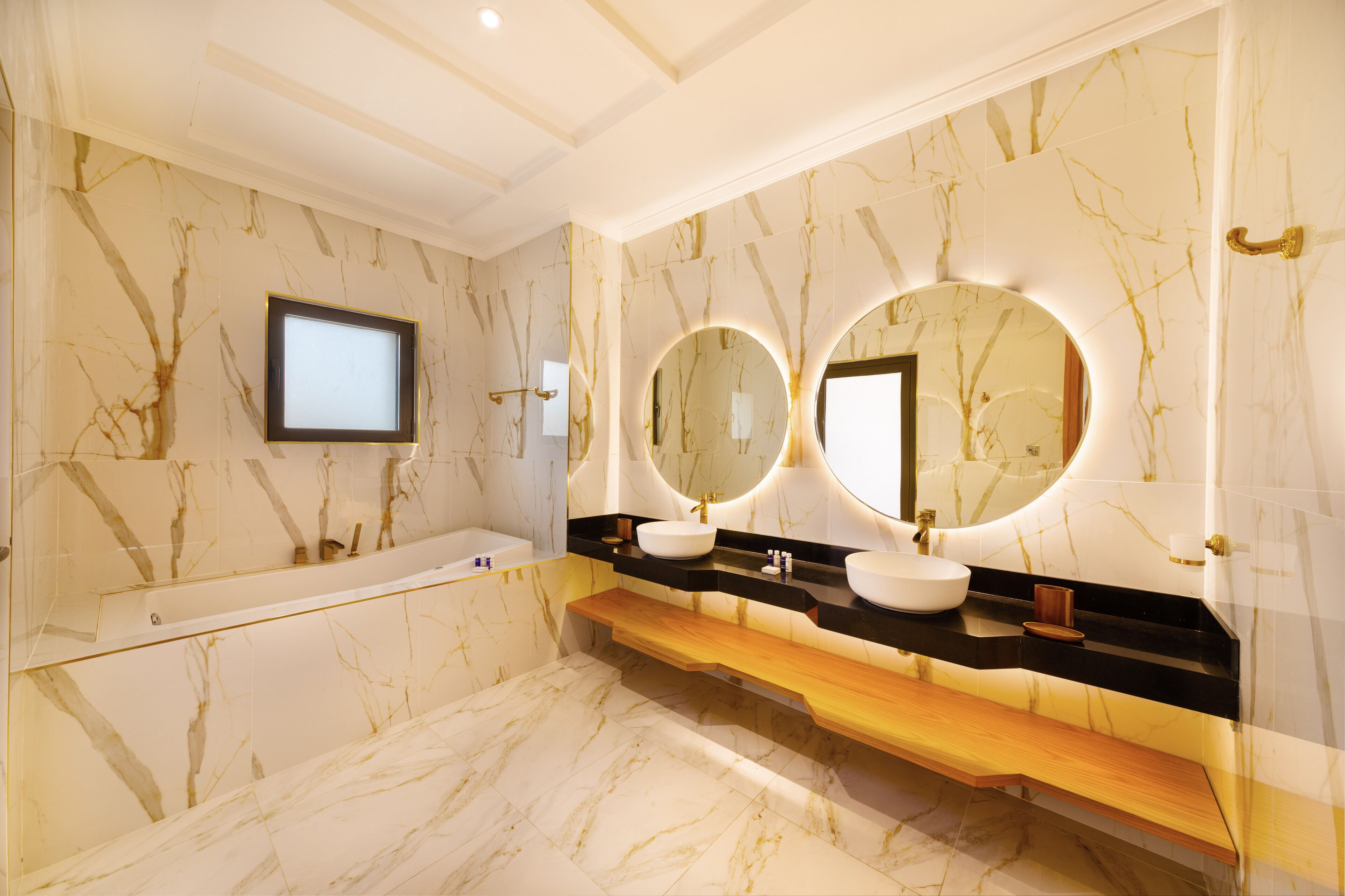 Une salle de bain luxueuse avec des murs en marbre, une grande baignoire et deux vasques agrémentées de miroirs ronds.