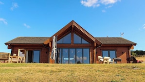 A two-story wooden cabin with large windows, a covered patio area, and outdoor seating. - Cuddfan Lodge on a Beautiful Lake (Newport)