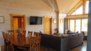 A spacious living area with a wooden dining table, chairs, a sofa, and a television mounted on the wall. - Cuddfan Lodge on a Beautiful Lake (Newport)
