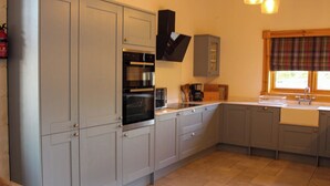 Una cocina con armarios grises, horno empotrado, cafetera y una ventana con cortina escocesa.
