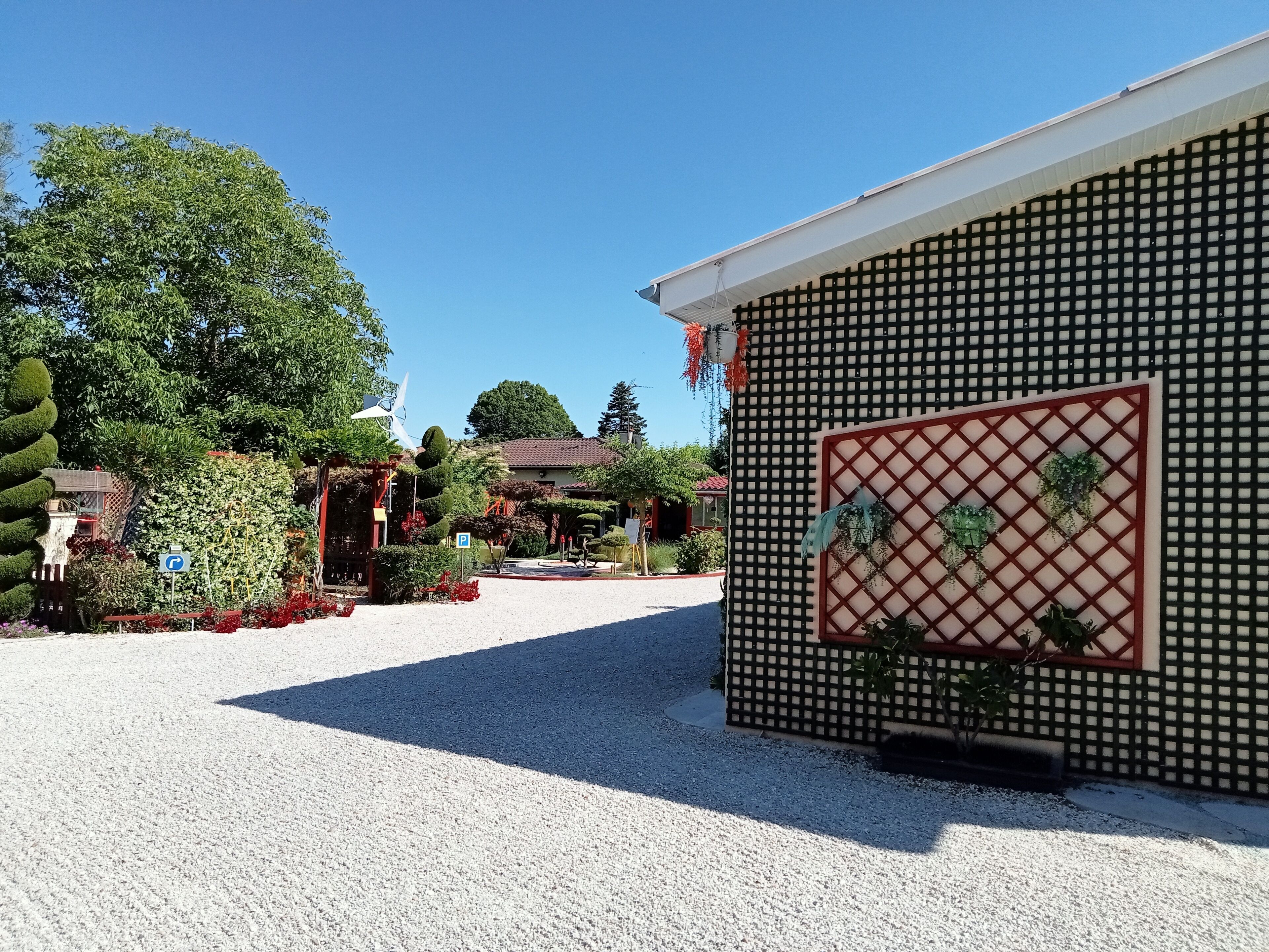 Un bâtiment dont la façade présente un motif en forme de quadrillage, une allée gravillonnée et un panneau indiquant un espace de stationnement.