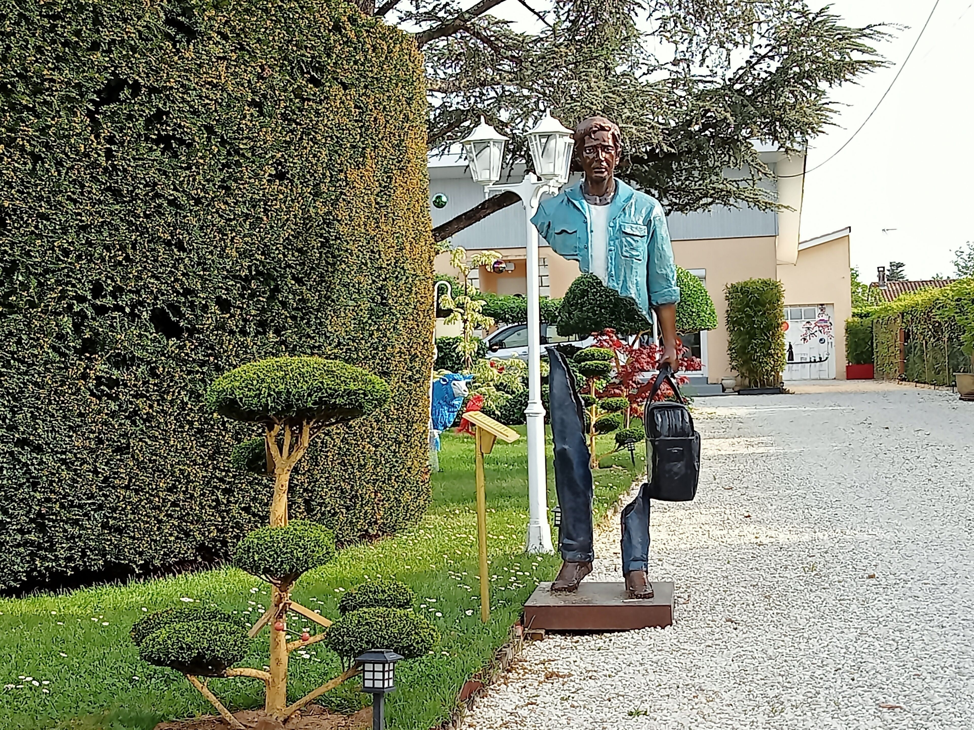 Eine Statue eines Mannes, der eine Tasche trägt, ein Laternenpfahl und ein kleiner Baum.