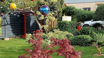 Un giardino con arbusti dal fogliame rosso, un albero decorato con ornamenti sferici appesi e un edificio sullo sfondo.
