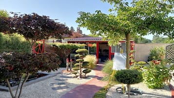Een tuin met een pad dat leidt naar een gebouw met een rood dak en een witte hekken.