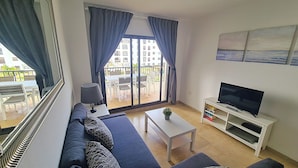 Een moderne woonkamer met een bank, een salontafel, een televisie op een meubel en een balkon met uitzicht op gebouwen.