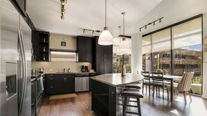 A modern kitchen with dark cabinets, stainless steel appliances, and a large island with bar stools. - Walkable Uptown Dallas 3BR with Pool, Pets, Wi-Fi (Dallas)