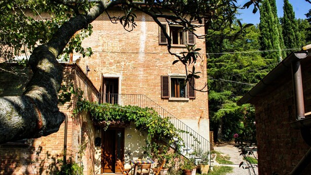 A rustic stone building with a balcony, a gravel path, and potted plants.