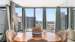 Un espace repas comprenant une table ronde, des chaises et une vue sur le paysage urbain, visible à travers de grandes fenêtres.