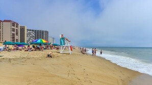 Une plage avec des parasols, une tour de surveillance pour les sauveteurs et des gens qui se détendent.