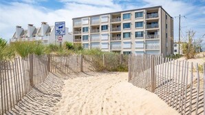 Un edificio a più piani con balconi, una spiaggia sabbiosa di fronte e un cartello che indica il numero civico 76.
