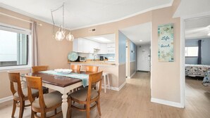 Una cucina moderna con mobili bianchi, una zona pranzo con sedie di legno e un corridoio che conduce a una camera da letto.