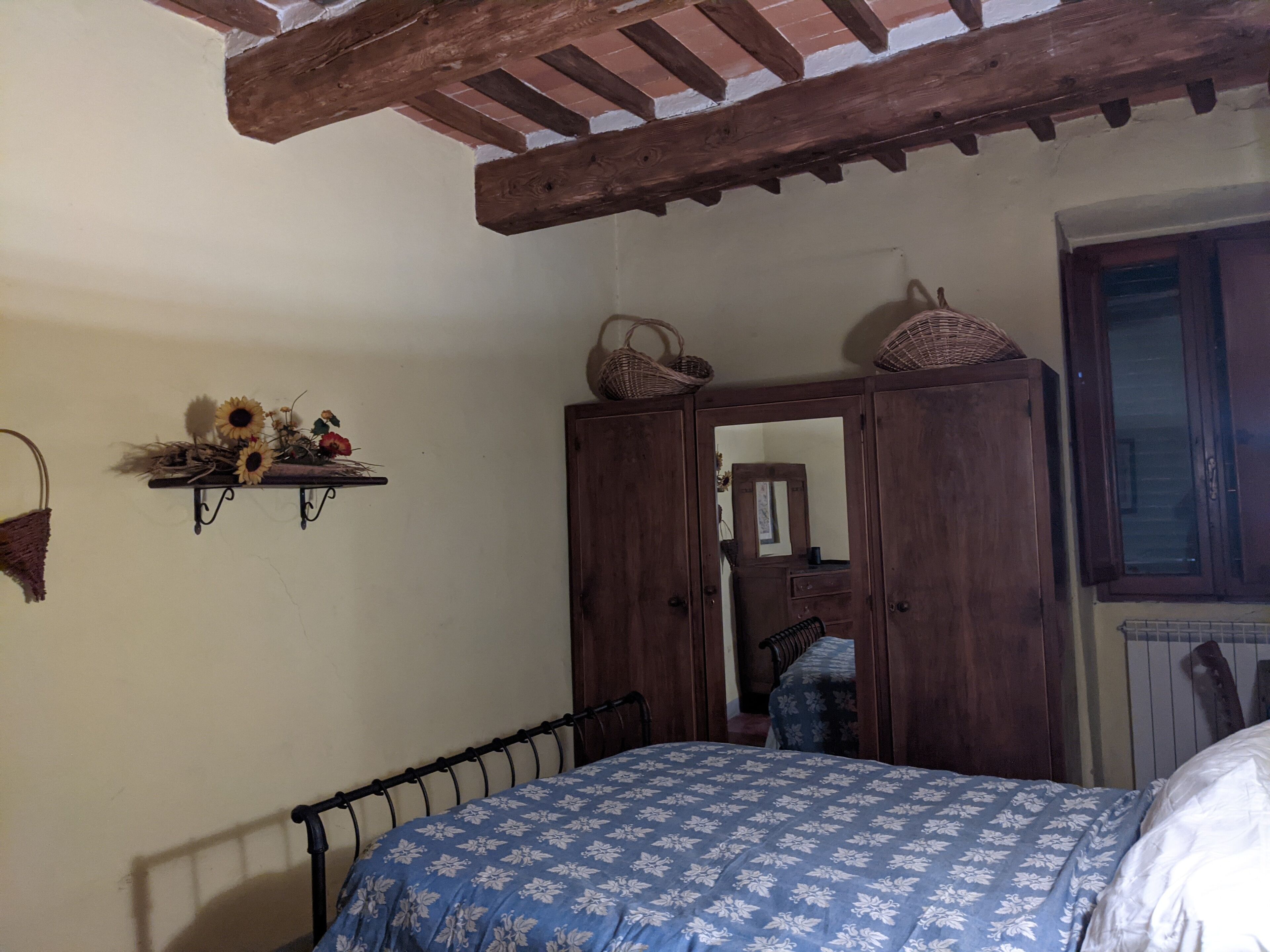 Une chambre à coucher avec un lit, une armoire en bois, une étagère avec des fleurs et une fenêtre.