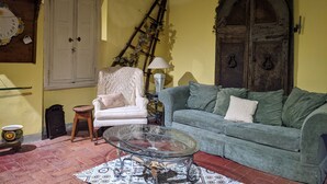 A cozy living room with a green sofa, a white armchair, a glass coffee table, and a rustic wooden door.
