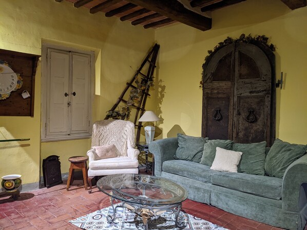 A cozy living room with a green sofa, a white armchair, a glass coffee table, and a rustic wooden door. - Casa Baldecchi - Pistoia Centro Storico (Pistoia)